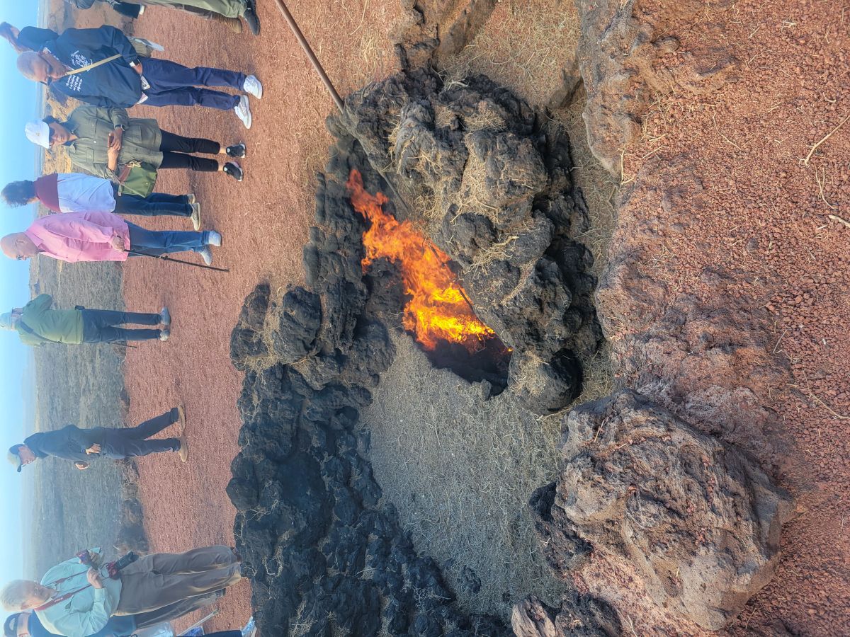 Flames rising from a hole in the volcanic ground at Timanfaya National Park, tourists watching from a safe distance