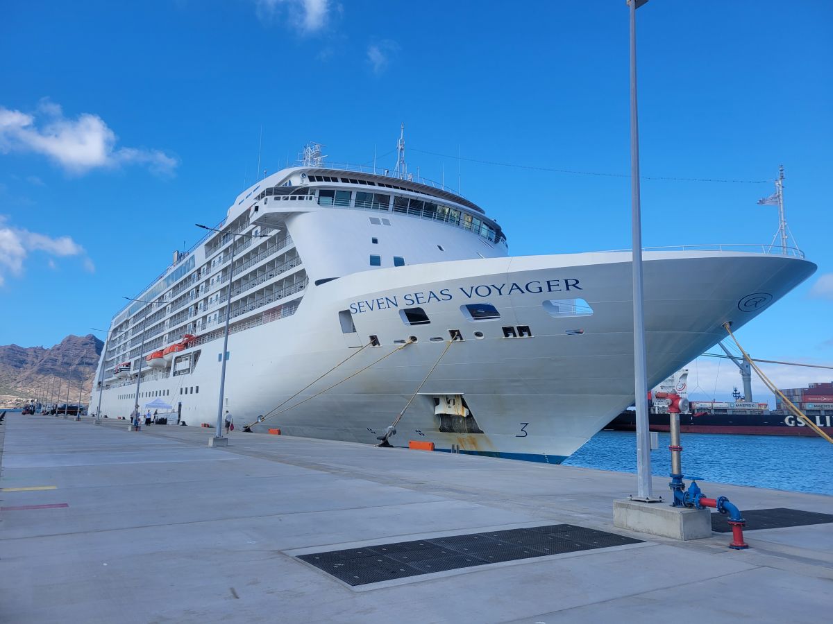 The Seven Seas Voyager docked in Mindelo harbor, her name visible on the hull, mountains of São Vicente rising behind