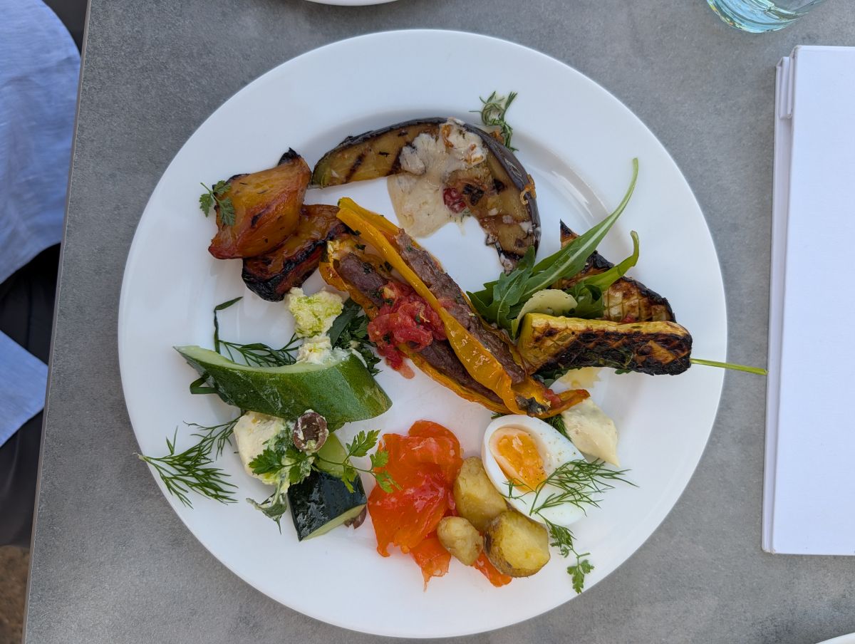 A Sunday Supper plate at Heckfield Place — charred and roasted vegetables including eggplant and peppers, smoked salmon, a soft-boiled egg, herbs and sauces, all estate-grown
