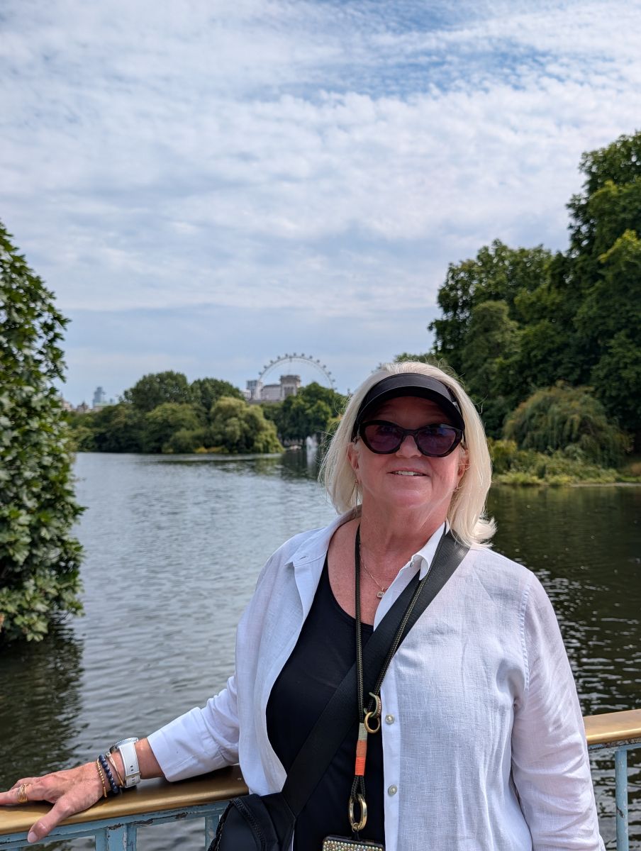 Shirley smiling on the bridge in St. James's Park, the London Eye visible in the distance through the trees, the park lake below