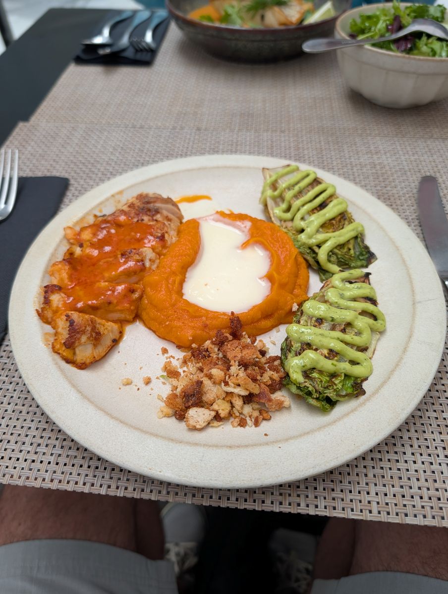 A beautifully plated fish dish with vibrant orange carrot puree and green vegetables